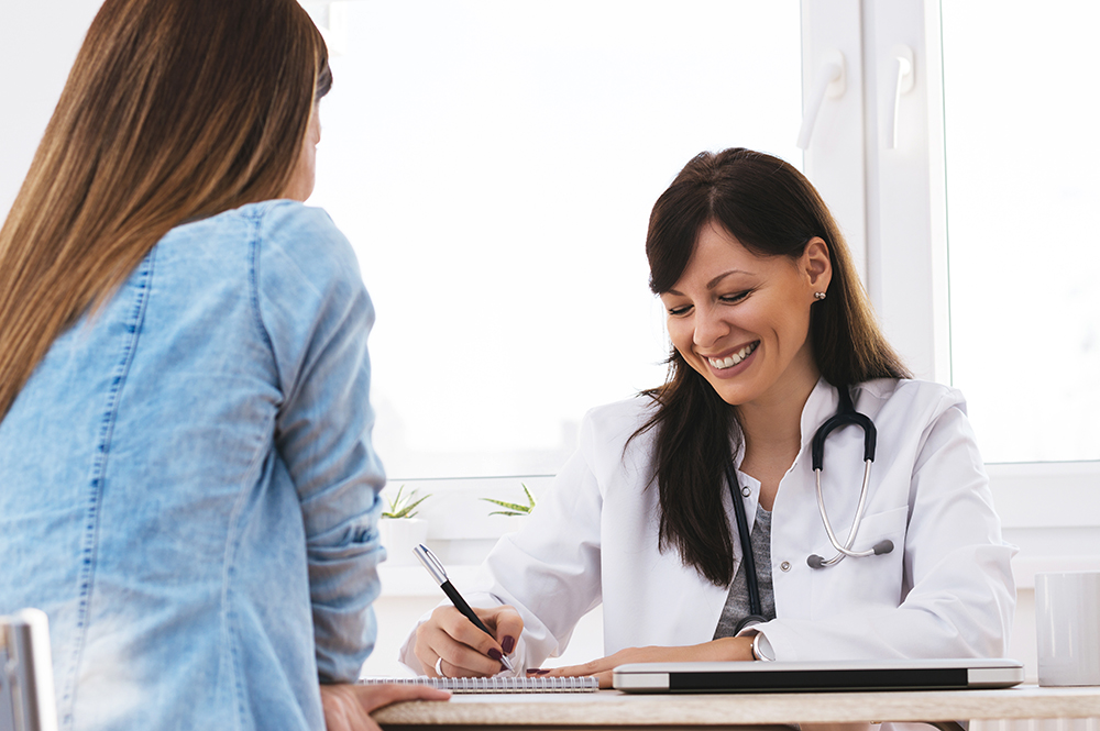 Smiling doctor having a funny conversation with patient. Beautiful female doctor writing report and smiling.